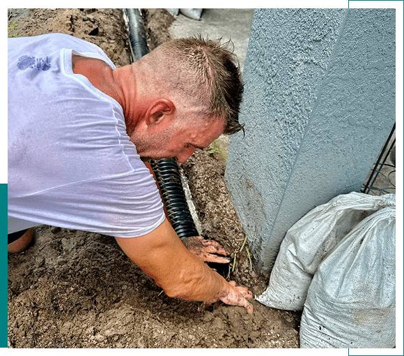 Man digging a hole in soil near a wall with a sandbag.