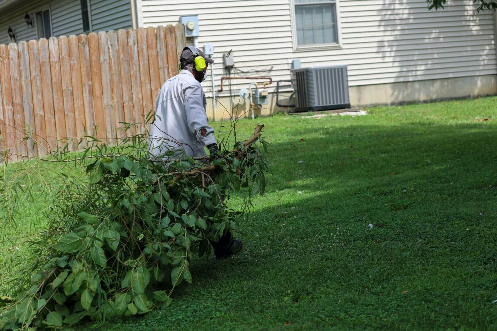Person wearing protective gear trimming bushes in a yard.