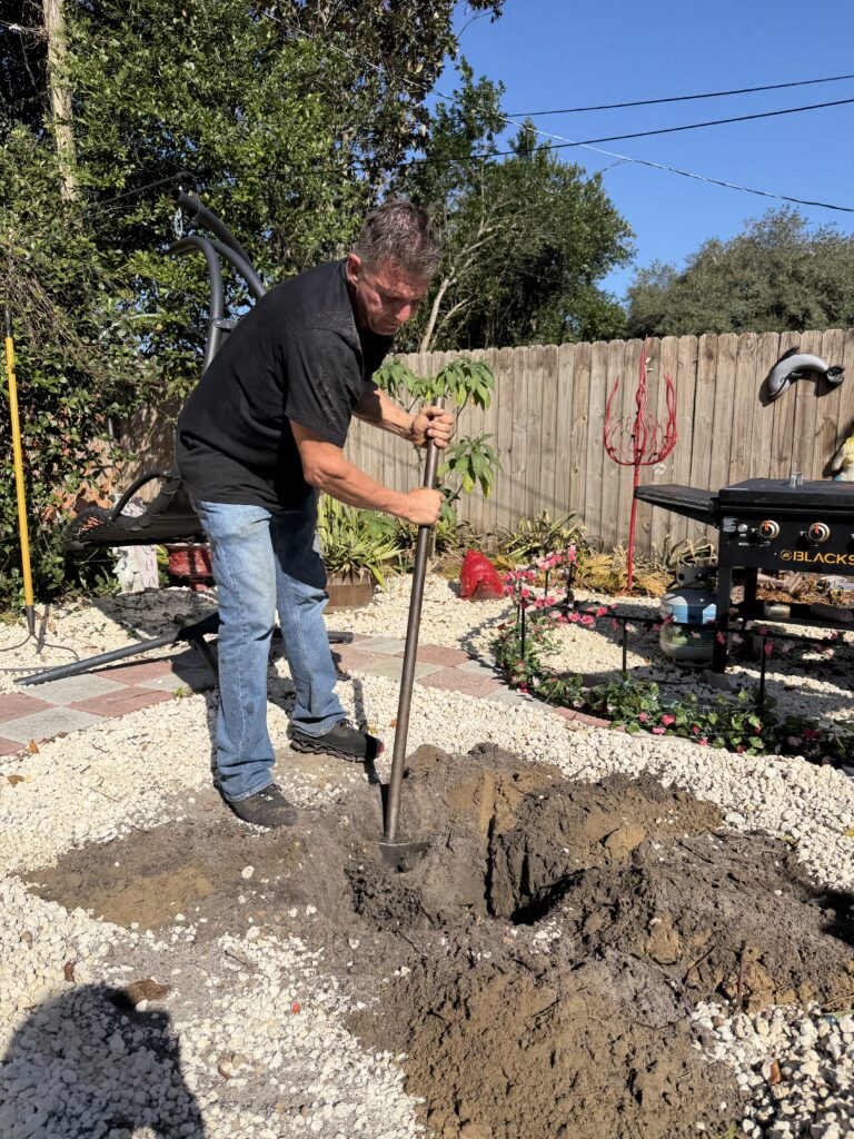 Man digging a large hole in a backyard with a shovel.